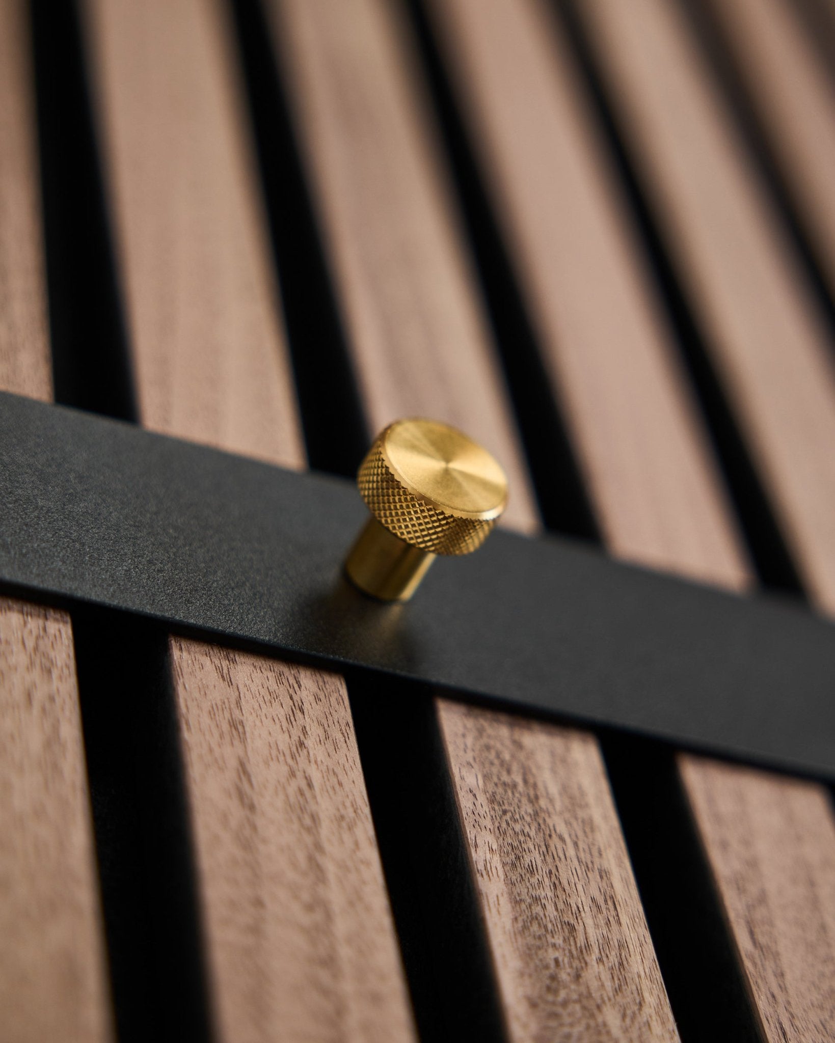 Wieszak Coat Hook Rack WoodUpp Norr ma siedem haczyków black z gałkami brass, zamocowanych na panelu lamelowym brown, zaprojektowanym jako nordycki dodatek do Akupanel.